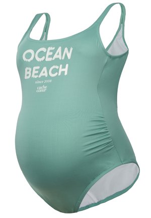 Maternity-Badeanzug in Teal mit weißem "OCEAN BEACH"-Text. Verfügt über verstellbare Träger, seitliche Raffungen für eine optimale Passform und ein glattes, dehnbares Material.