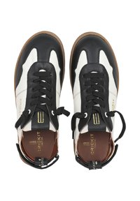 Scarpe in pelle bianco e nero con un design sportivo, dotate di lacci neri e accenti, suola marrone e branding dorato ai lati.
