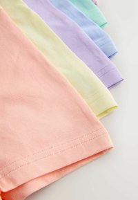 Złożona bawełniana tkanina w pastelowych kolorach, w tym morelowym, żółtym, lawendowym, jasnoniebieskim i miętowozielonym, ułożona nachodząco na białej powierzchni.