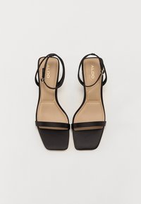 Paire de sandales noires à lanières, bouts carrés et brides à la cheville sur fond blanc uni.