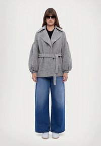 Hall hallisegu vildist jakk laiade kraedega, vöödiga talje ja volüümikate varrukatega, millele on lisatud sinised laia jalaga teksad ja valged tennised.