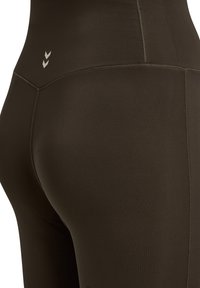 Brązowe legginsy z wysokim stanem, elastyczne, o gładkiej fakturze, z trzema małymi białymi chevronami z tyłu i szwami płaskimi.