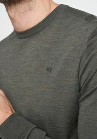 Maglione a maniche lunghe di colore verde scuro con scollo a girocollo, caratterizzato da un punto tessuto testurizzato, e un piccolo dettaglio ricamato con "#3" sul petto.