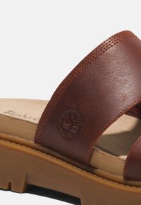 Sandali in pelle marrone con cinghie incrociate, superficie testurizzata e una soletta imbottita color tan con logo impresso su una cinghia.