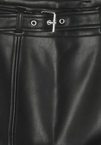 Gros plan d'une jupe en cuir noire avec une ceinture à boucle argentée et des coutures visibles sur le côté gauche.