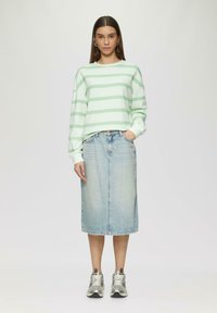 Felpa oversize a righe verde chiaro, gonna di jeans blu di lunghezza media e sneakers argentate. Materiali semplici con elementi di design informale.