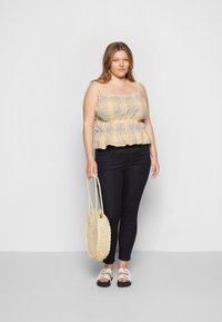 Top peplum em padrão gingham nas tonalidades de amarelo pastel e azul, com detalhes franzidos e alças finas, combinado com jeans skinny escuros e uma bolsa de palha.