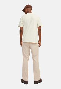 Lys beige kortærmet t-shirt med en afslappet pasform, parret med lys beige bukser. Bagfra vises et enkelt design og flade sømme.