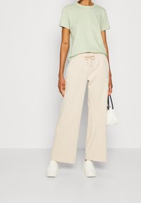 Light green short-sleeve t-shirt with small logo, paired with loose beige sweatpants featuring an elastic waistband and side pockets. White sneakers.