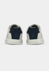 Κομψά sneakers unisex με μπεζ σώμα από σουέντ, ναυτικά σκούρα στοιχεία και λευκή λαστιχένια σόλα με λογότυπο στο πίσω μέρος.