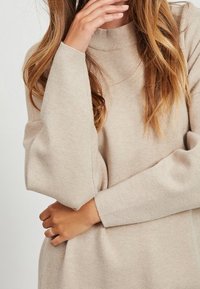Maglione beige con colletto alto a coste e maniche lunghe e morbide. Realizzato in un tessuto morbido e testurizzato, presenta una silhouette rilassata.