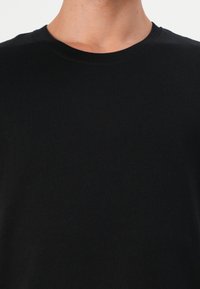 Tricou negru din bumbac, cu guler rotund, mâneci scurte și o textură netedă, fără modele vizibile sau detalii metalice.