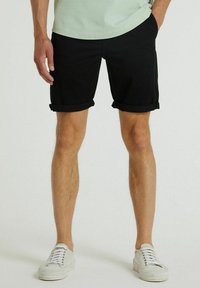 Shorts di cotone neri con risvolti, abbinati a sneakers in tela bianche. I pantaloni presentano una vestibilità comoda e tasche laterali.