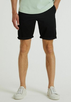 Zwarte katoenen shorts met opgerolde zomen, gecombineerd met witte canvas sneakers. De shorts hebben een vaste pasvorm en zijzakken.