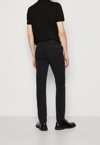 Black polo shirt with short sleeves, viewed from the back. Paired with slim-fit black pants and shiny black shoes.