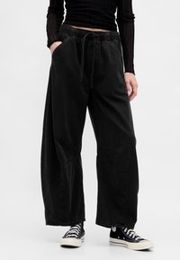 Pantaloni neri a gamba larga in morbido cotone, con vita elasticizzata e coulisse, due tasche laterali e dettagli di cuciture sottili.