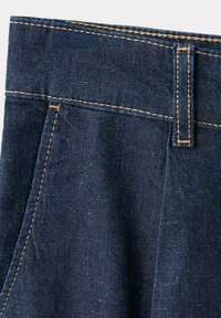 Close-up of dark blue denim fabric showing waistband, belt loop, and pocket with contrasting orange stitching.