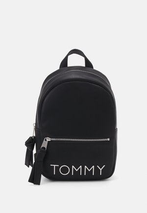 Czarny plecak z przednią kieszenią na zamek, srebrnym zamkiem, materiałowymi frędzlami przy suwaku oraz logo "TOMMY" białymi literami z przodu.