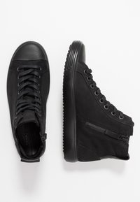 Black high-top shoes made of leather and rubber. Features include round toe, lace-up front, and side zipper. Textured sole for grip.