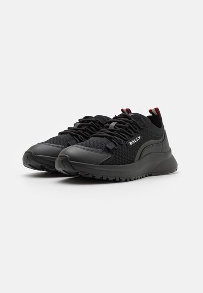 Scarpe da ginnastica nere con tomaia in rete strutturata, suola in gomma solida, design imbottito e linguetta rossa sul tallone.
