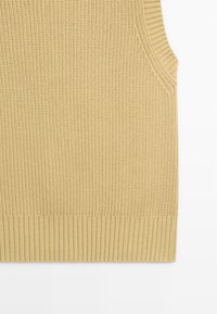 Gilet sans manches tricoté beige avec ourlet côtelé et motif de points verticaux texturés.