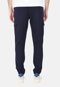 Pantaloni cargo blu navy con tasche laterali, design affusolato, texture del tessuto morbida e polsini elasticizzati; indossati con sneakers bianche e dettagli blu.