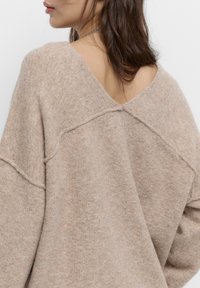 Beige oversized sweater med V-hals, blød tekstur, løs pasform og synlige syninger langs bagsømmen.