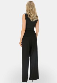 Czarny kombinezon bez rękawów z dopasowaną górą i szerokimi spodniami. Posiada kieszenie po bokach i gładką teksturę materiału.