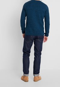 Pull bleu tricoté avec un motif texturé, associé à un jean denim foncé. Bottes en daim couleur tan avec revers roulés complètent le look.
