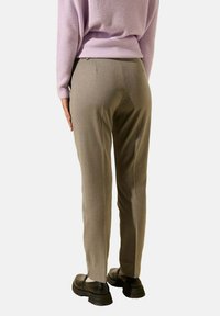Pantalons beige ajustés avec une coupe slim, présentant une texture lisse et de discrètes poches arrière, associés à un pull en lilas à côtes.