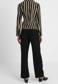 Haut ajusté à rayures verticales noires et crème, manches longues, col haut, avec un pantalon large noir assorti orné de boutons sur les côtés.