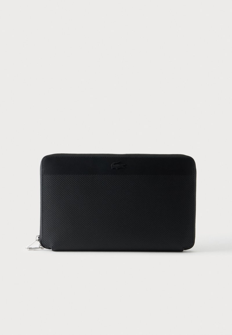 Portefeuille noir texturé avec fermeture éclair tout autour, bande supérieure en cuir lisse et logo crocodile embossé à l'avant.