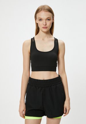 Sort sportstop med gennemsigtige skulderdetaljer, parret med sorte shorts med neongrønne detaljer. Glat tekstur, tætsiddende design.