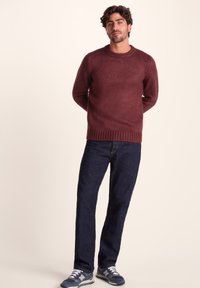 Maroon knit sweater with crew neckline, ribbed hem and cuffs; paired with dark blue jeans and navy sneakers with white accents.