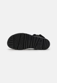 Suela de zapato de goma negra con textura, que presenta surcos y crestas para proporcionar tracción. Sin logotipos ni patrones visibles.