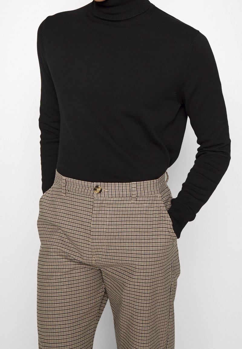 Pull noir à col roulé associé à un pantalon taille haute à motif pied-de-poule, avec fermeture à boutons et poches latérales.