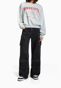 Harmaa huppari, jossa on punainen "Minnesota 86" -teksti, yhdistetty mustiin cargo-housuihin, joissa on useita taskuja ja löysä istuvuus. Mustavalkoiset lenkkarit.