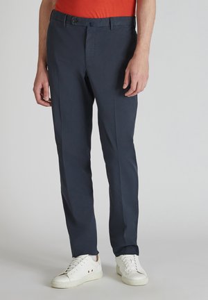 Pantalon bleu marine en tissu léger, avec une coupe droite, des passants de ceinture et une fermeture à bouton. Porté avec des baskets blanches.