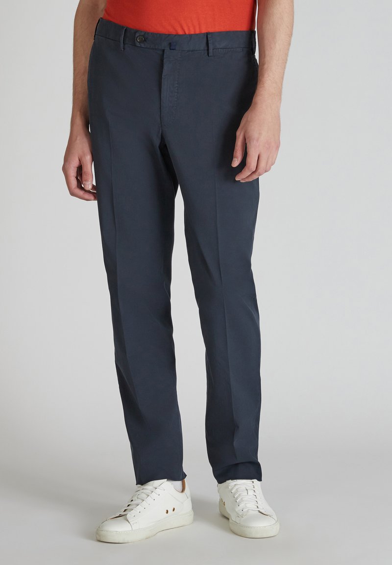 Pantaloni blu navy realizzati in un tessuto leggero, con un taglio dritto, passanti per la cintura e chiusura con bottone. Indossati con scarpe da ginnastica bianche.