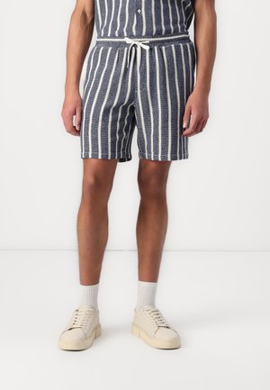 Navy and white striped shorts with an elastic waistband and drawstring, made from textured fabric. Worn with light-colored sneakers and socks.