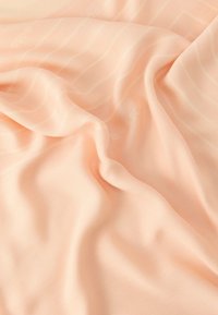 Pehme virsikuvärvi kangas, millel on õrnad vertikaalsed triibud ja õrnad voldid, luues sujuva, voolava tekstuuri.