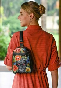 Zwarte leren rugzak met kleurrijke bloemenontwerpen en een schedelmotief, met een afgeronde vorm en een enkele verstelbare schouderband.