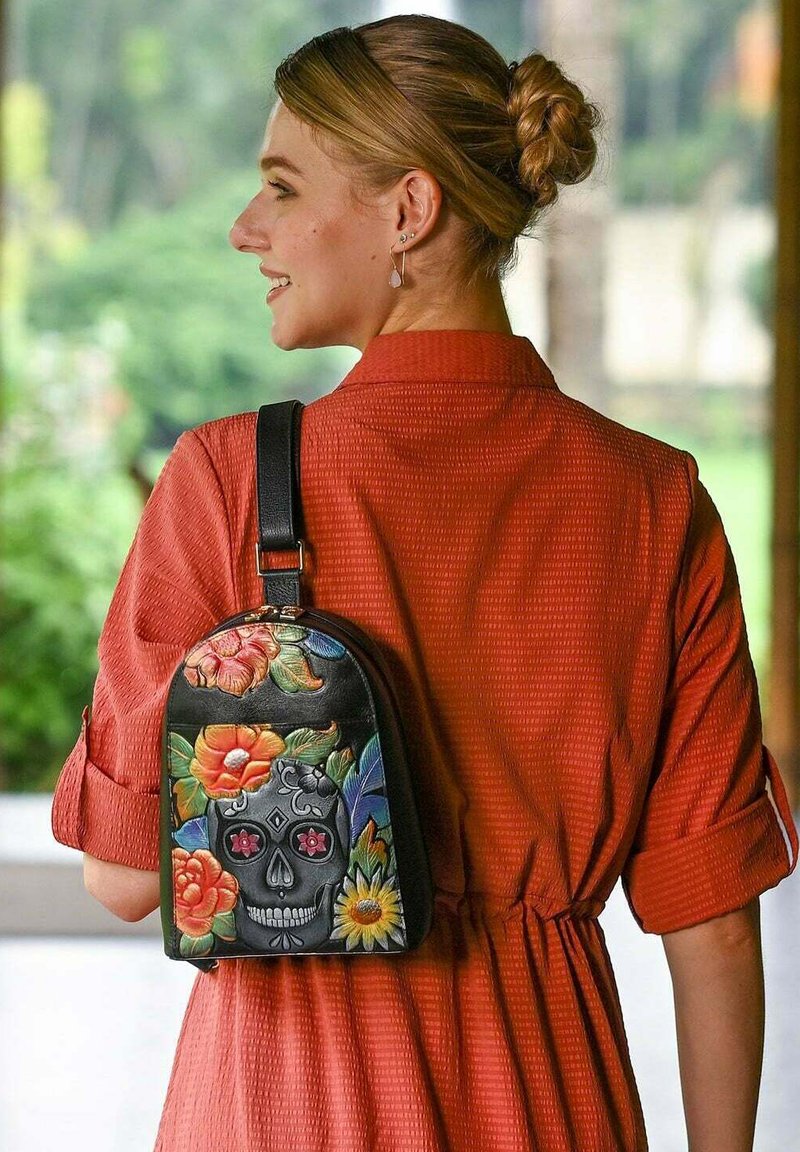 Zwarte leren rugzak met kleurrijke bloemenontwerpen en een schedelmotief, met een afgeronde vorm en een enkele verstelbare schouderband.