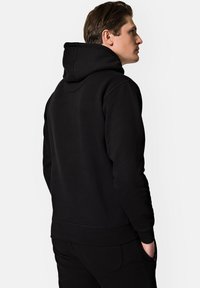 Czarna bluza z kapturem, z kieszenią typu kangur i regulowanym kapturem na sznurku. Gładka tekstura i ściągacze na mankietach, widok z tyłu.