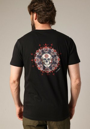 Zwarte katoenen t-shirt met een centraal schedelontwerp omringd door ingewikkelde rode en blauwe bloempatronen. Korte mouwen en ronde hals.