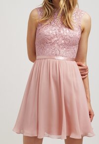 Robe rose avec un corsage en dentelle ajusté orné de sequins et une jupe en chiffon évasée, accentuée d'une ceinture en satin.