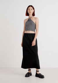 Γκρι κοντό halter top με λεπτομέρεια ροζ, συνδυασμένο με μια μαύρη maxi φούστα και χοντρές μαύρες σανδάλια. Λείες υφές και μινιμαλιστικός σχεδιασμός.