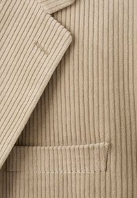 Beige corduroy fabric with ribbed texture, featuring a notched collar and a small pocket. Gold stitching detail near the lapel.