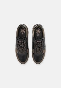 Black and brown sneakers with a textured surface, featuring a wide toe box, contrasting laces, and logo accents on the tongue and side.