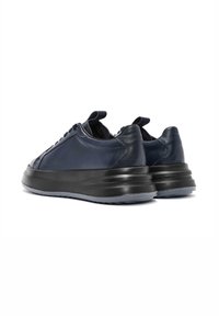 Zapatillas de cuero navy con suela negra gruesa. Forma redondeada, diseño minimalista y acentos texturizados en la parte superior. Tablas de doble tirador en la parte trasera.